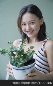 Portrait of a young woman holding a potted plant and smiling