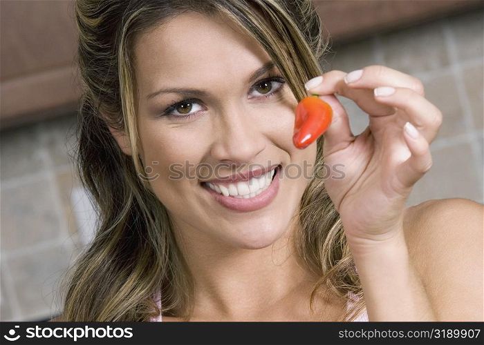 Portrait of a young woman holding a red chili pepper and smiling