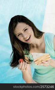 Portrait of a young woman holding a sandwich and a tomato