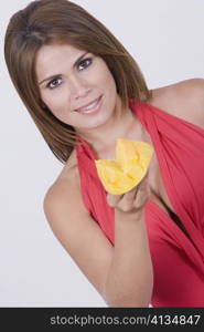 Portrait of a young woman holding a slice of mango and smiling