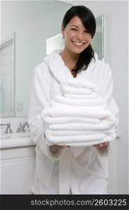 Portrait of a young woman holding a stack of towels and smiling