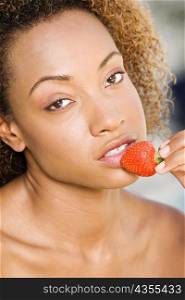 Portrait of a young woman holding a strawberry close to her mouth