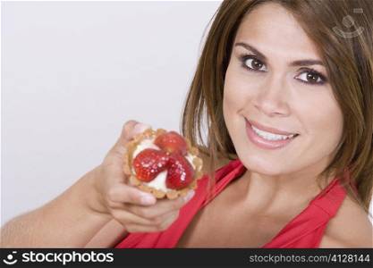 Portrait of a young woman holding a strawberry tart and smiling