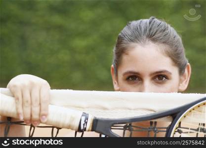 Portrait of a young woman holding a tennis racket over a tennis net