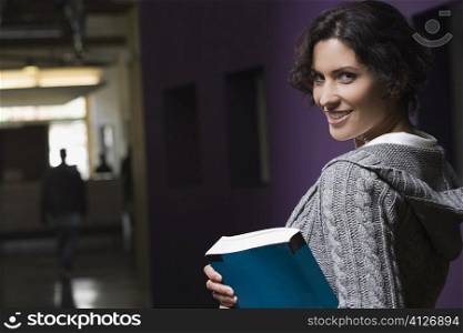 Portrait of a young woman holding a textbook and smiling