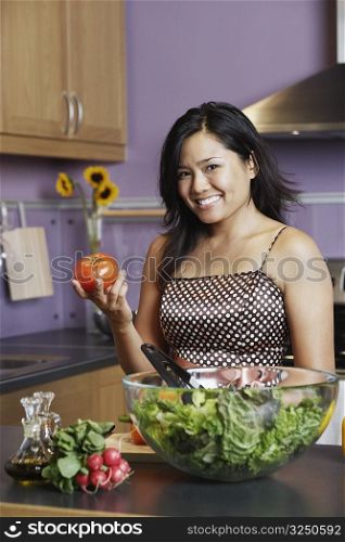 Portrait of a young woman holding a tomato in the kitchen