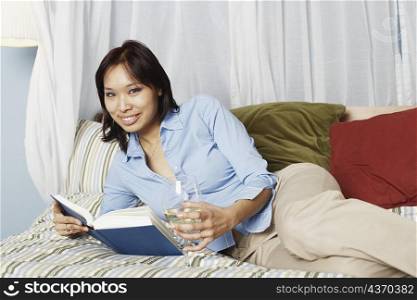 Portrait of a young woman holding a wineglass and a book on the bed