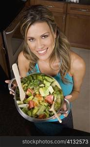 Portrait of a young woman holding a wok of salad in the kitchen