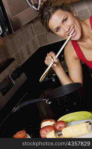 Portrait of a young woman holding a wooden spoon in her mouth and smiling in the kitchen