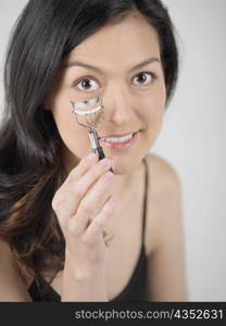 Portrait of a young woman holding an eyelash curler