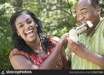 Portrait of a young woman holding an ice cream and a mid adult man eating it