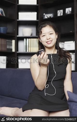 Portrait of a young woman holding an MP3 player listening to music on headphones