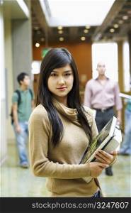 Portrait of a young woman holding books and standing in the corridor