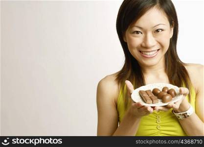 Portrait of a young woman holding chocolates in a plate and smiling