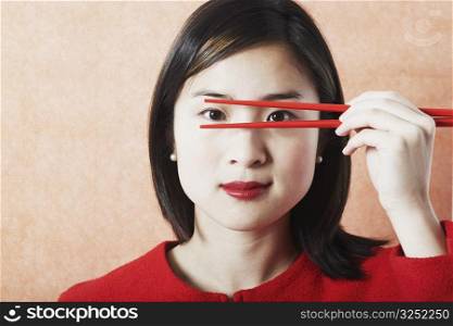 Portrait of a young woman holding chopsticks in front of her face