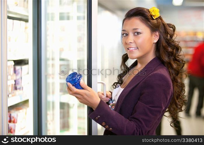 Portrait of a young woman holding container in front of refrigerator in the supermarket