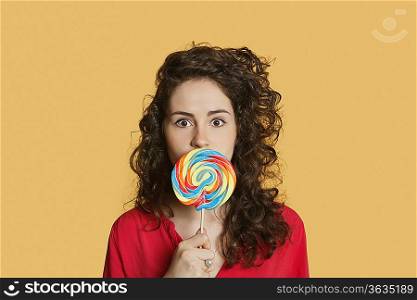 Portrait of a young woman holding lollipop in front of face over colored background
