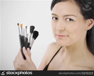 Portrait of a young woman holding make-up brushes