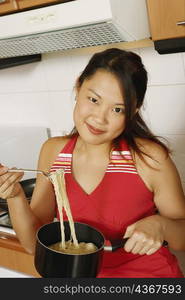 Portrait of a young woman holding noodles with a fork at a kitchen counter