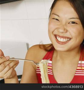 Portrait of a young woman holding noodles with a fork at a kitchen counter