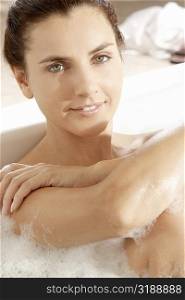 Portrait of a young woman hugging her knees in a bathtub and smiling