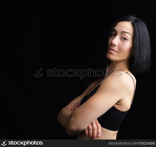 portrait of a young woman in a black sports bra on a dark background, girl looking at the camera