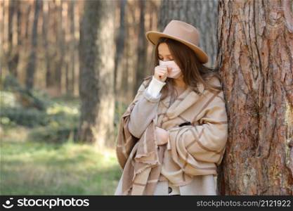 Portrait of a young woman in a hat and medical mask with a protective face who coughs in the park on a sunny day. The virus spreads quarantine to prevent the flu. Portrait of a young woman in a hat and medical mask with a protective face who coughs in the park on a sunny day. The virus spreads quarantine to prevent the flu.