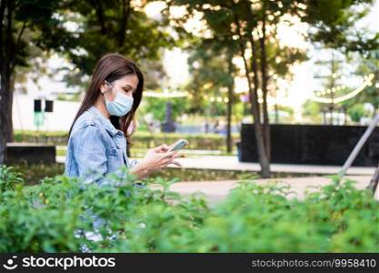 Portrait of a young woman in a medical mask for anti-coronavirus COVID-19 pandemic infectious disease outbreak protection and use a smartphone in Public area. Concept of Virus pandemic and pollution