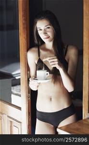 Portrait of a young woman in lingerie dipping a teabag in a cup of tea