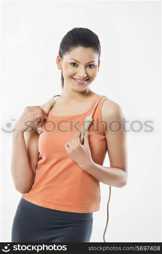Portrait of a young woman in sportswear holding jump rope over white background