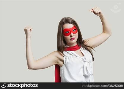 Portrait of a young woman in super hero costume flexing muscles over gray background