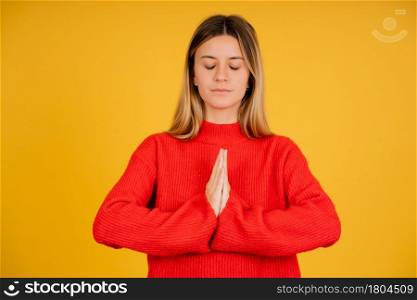 Portrait of a young woman keeping hands together in a zen and meditation gesture while standing against isolated background. Enjoys peaceful atmosphere for good relaxation.