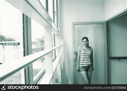Portrait of a young woman leaning against a door and smiling