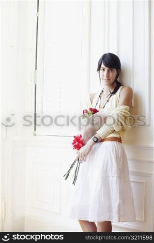 Portrait of a young woman leaning against a wall and holding a bouquet of flowers