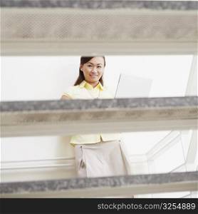 Portrait of a young woman leaning against a wall and using a laptop