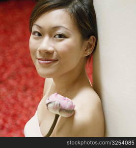 Portrait of a young woman leaning against a wall near a hot tub filled with rose petals