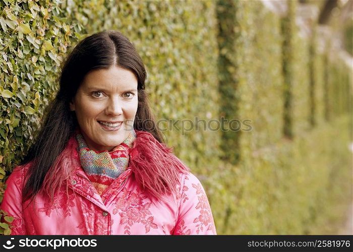 Portrait of a young woman leaning against an ivy covered wall and smiling