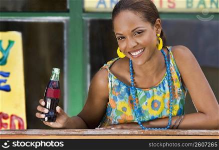 Portrait of a young woman leaning on a railing and holding a cola bottle
