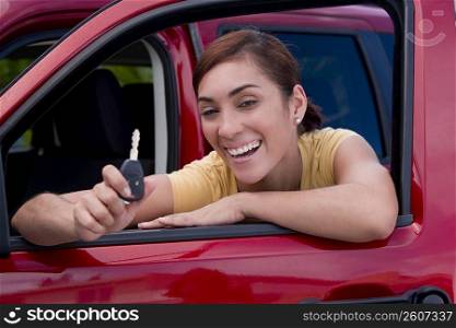 Portrait of a young woman leaning on the window of a car and showing a car key