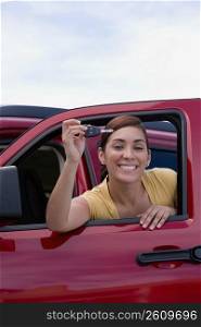 Portrait of a young woman leaning on the window of a car and showing a car key