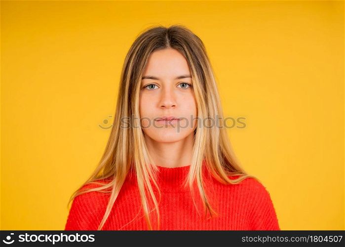 Portrait of a young woman looking at the camera while standing against yellow background.