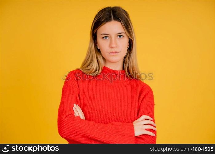 Portrait of a young woman looking serious to the camera with crossing arms while standing against yellow background.