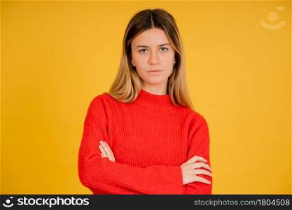 Portrait of a young woman looking serious to the camera with crossing arms while standing against yellow background.