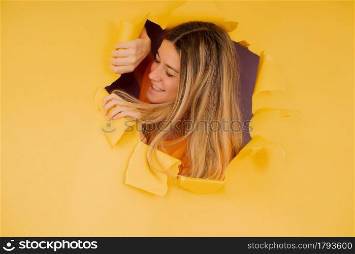 Portrait of a young woman looking through a torn hole in a paper wall.