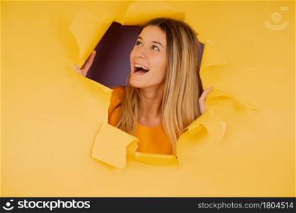 Portrait of a young woman looking through a torn hole in a paper wall.