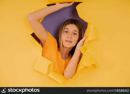 Portrait of a young woman looking through a torn hole in paper wall.