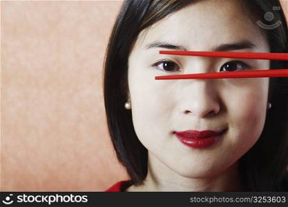 Portrait of a young woman looking through chopsticks