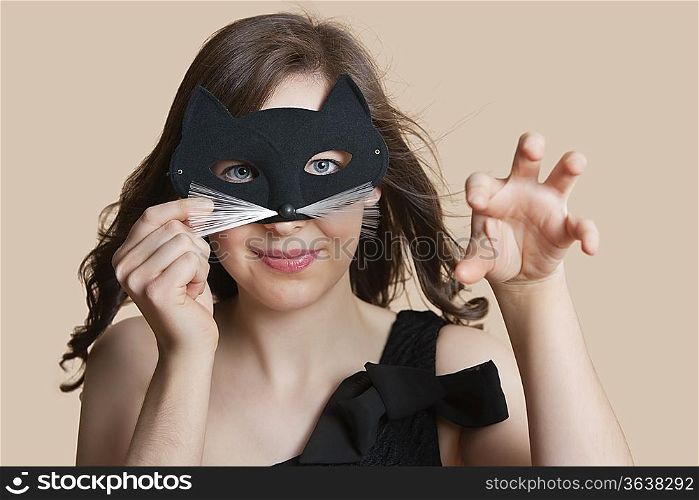 Portrait of a young woman looking through eye mask imitating as cat over colored background