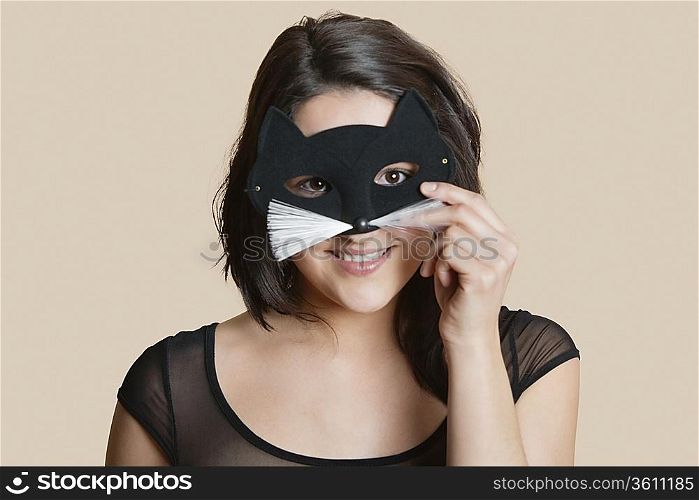 Portrait of a young woman looking through eye mask over colored background