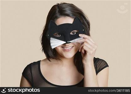 Portrait of a young woman looking through eye mask over colored background